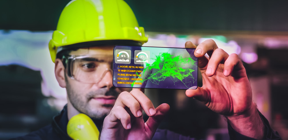A construction worker wearing a hard hat and safety glasses uses a futuristic transparent smartphone to interact with an AR/VR design of a building.